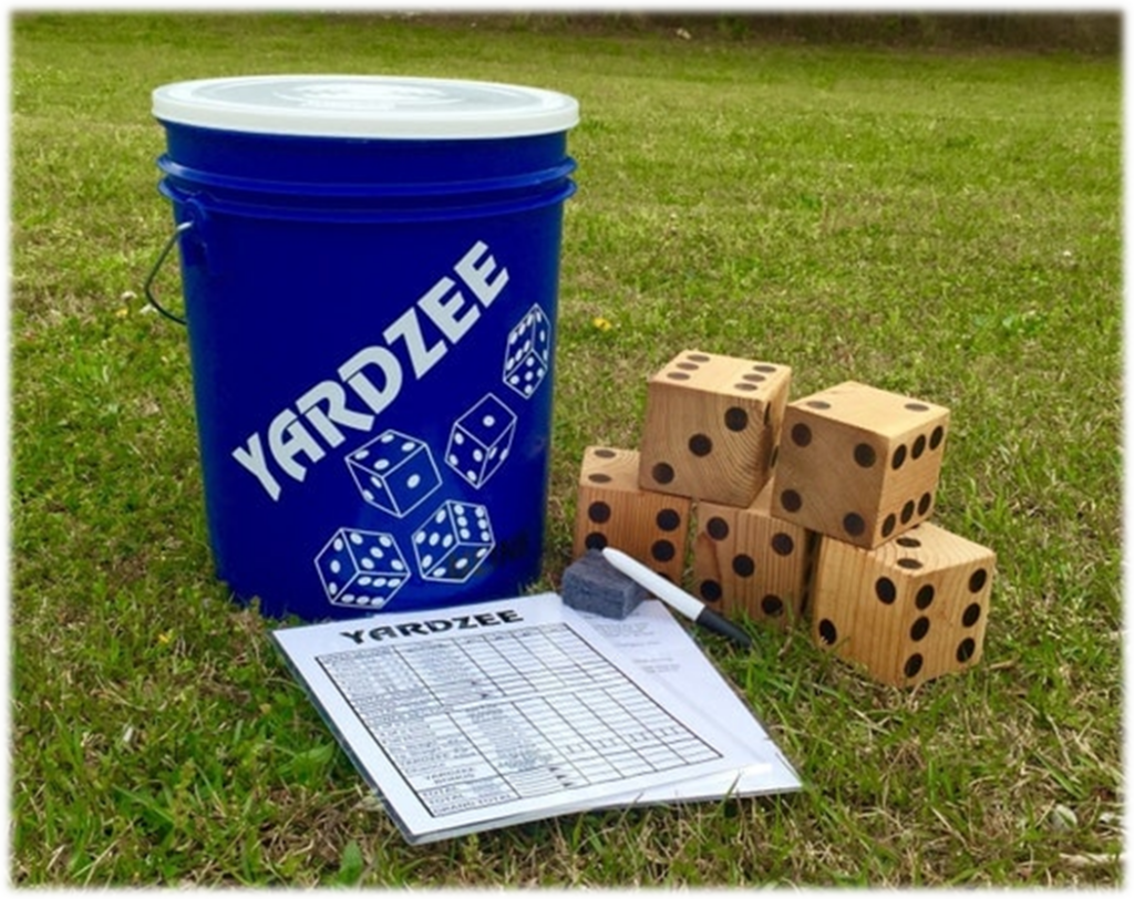 A Yardzee lawn game set is showcased on the main grass. The set includes a blue bucket labeled "YARDZEE" with dice images, five large wooden dice, a laminated score sheet, a dry erase marker, and an eraser for endless Yard Yahtzee fun.