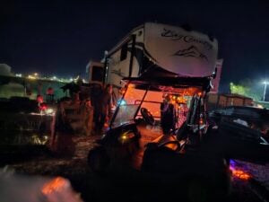A nighttime scene emerges with a large RV adorned in string lights, resembling a gallery of twinkling stars. In front, a golf cart is parked. People gather nearby, crafting a festive atmosphere awash in conviviality and charm.