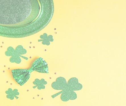 A glittery green top hat, shamrock shapes, and a green sequin bow tie are scattered on a pale yellow background, along with small sparkling stones, adding a festive touch reminiscent of President's Day celebrations.