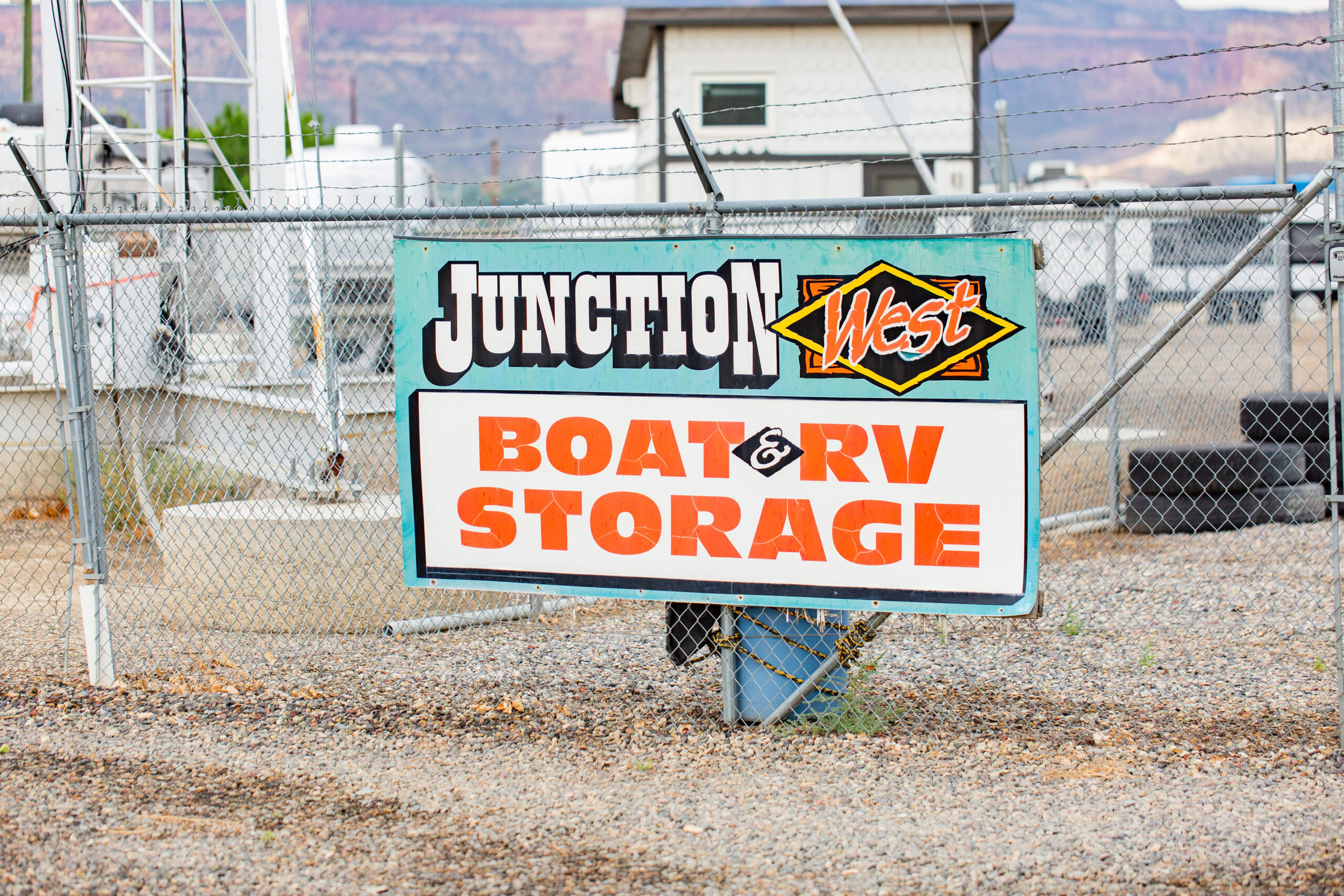 A sign on a chain-link fence reads "Junction West Boat & RV Storage" at an outdoor storage facility.