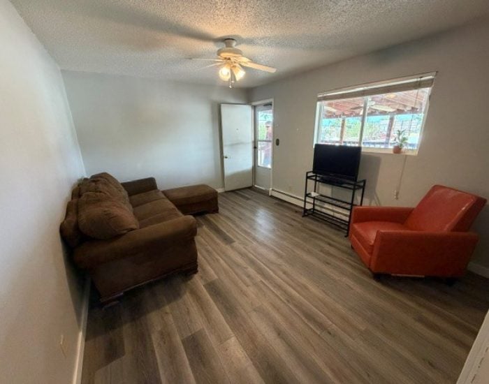 Living room with a brown sectional sofa, a red armchair, a television on a stand, and a ceiling fan.