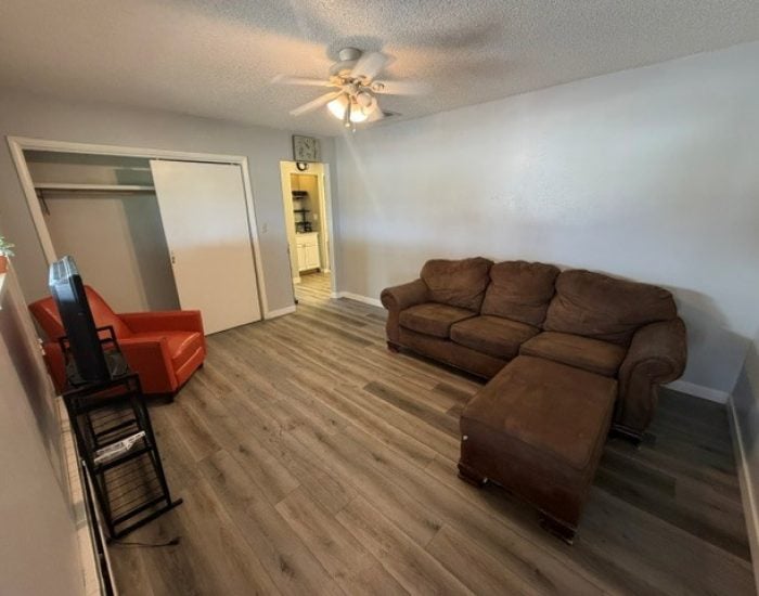 A living room featuring a brown sectional sofa with an ottoman, an orange armchair, and a TV stand.